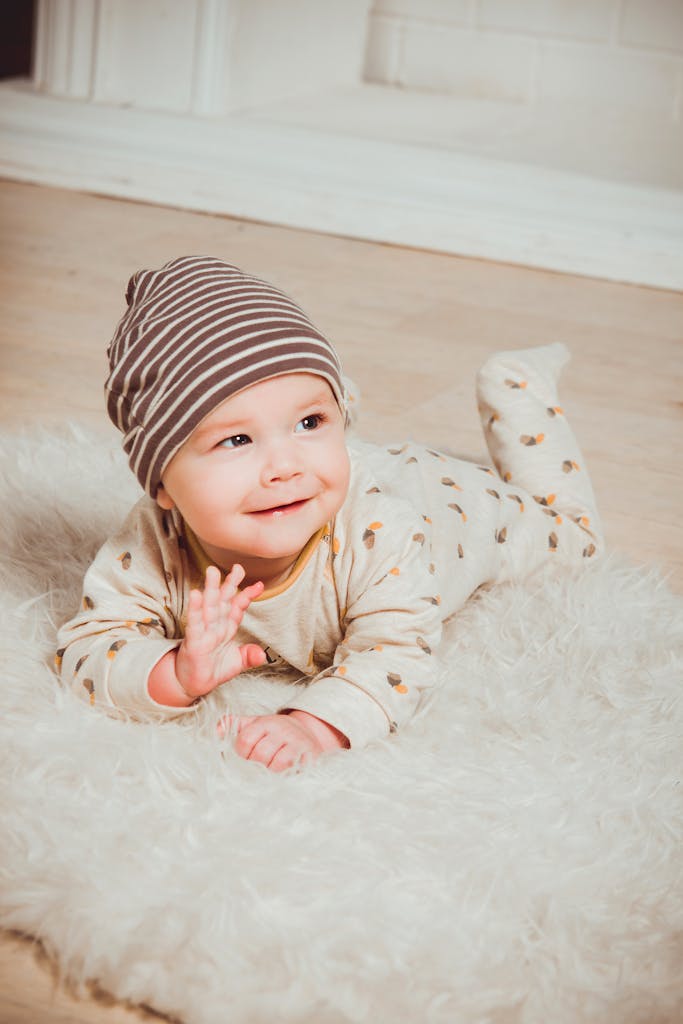 A cute baby in striped beanie lying on fluffy rug indoors, smiling with innocence.