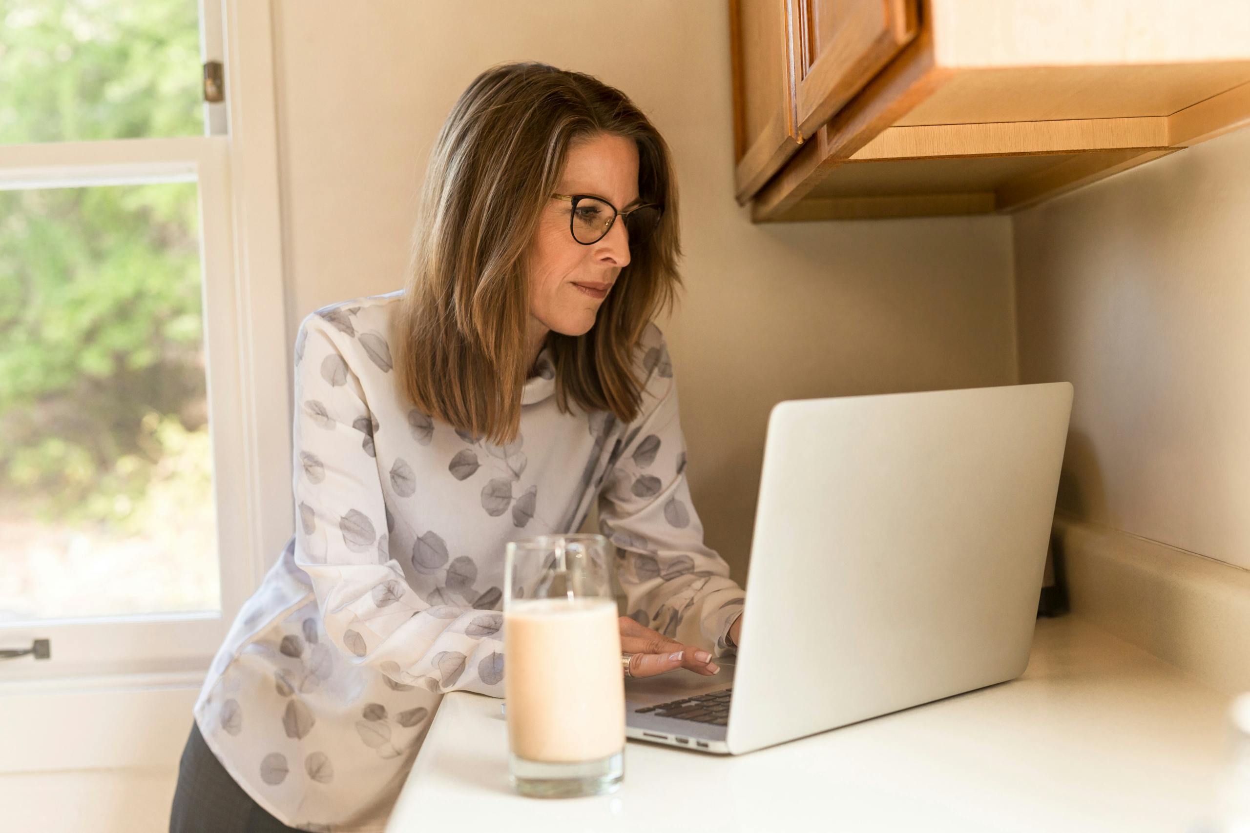 A woman working on a laptop in a home kitchen, illustrating remote work lifestyle.