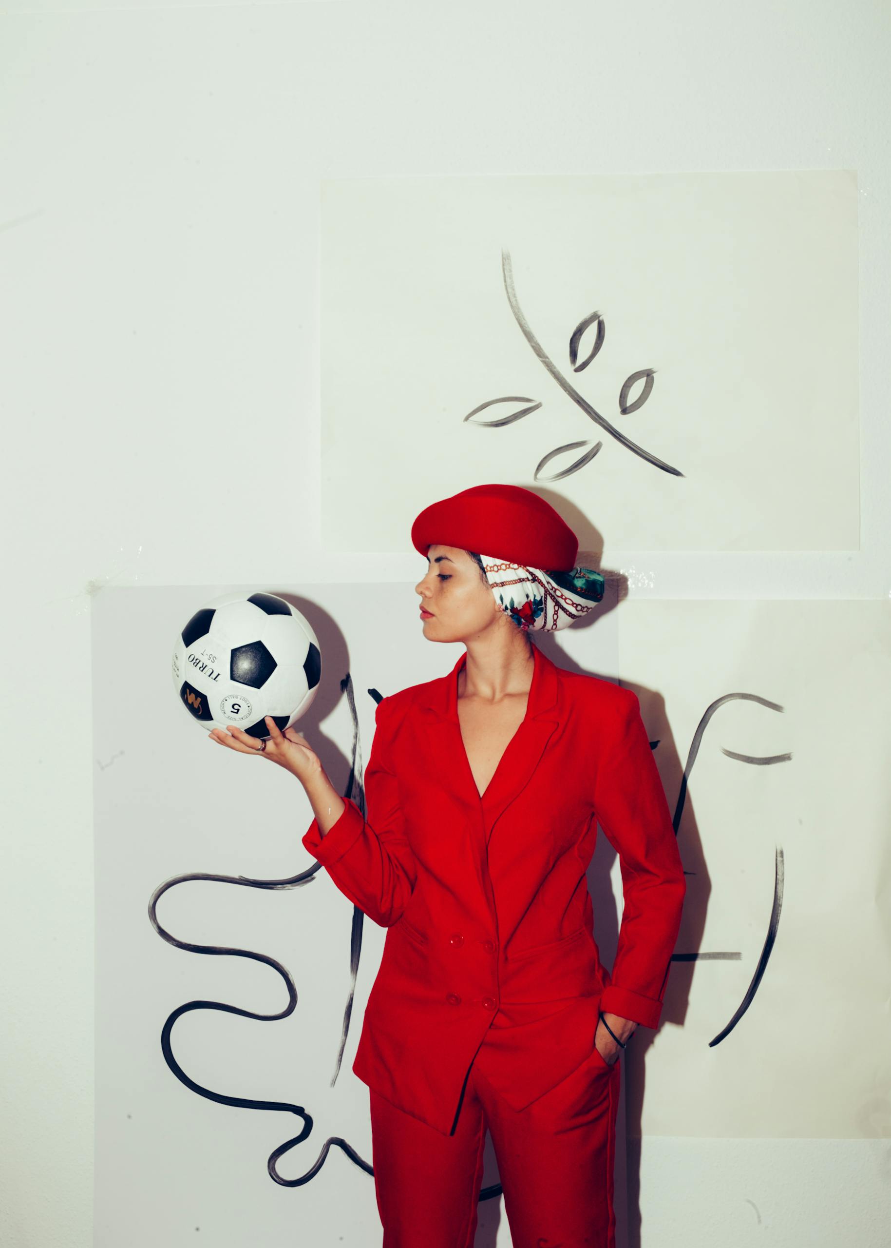 Confident woman in red suit holding a soccer ball, showcasing style and individuality.