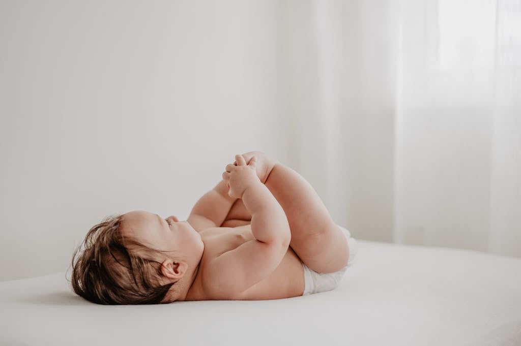 A baby lies peacefully on a bed, bathed in soft natural light from a nearby window.