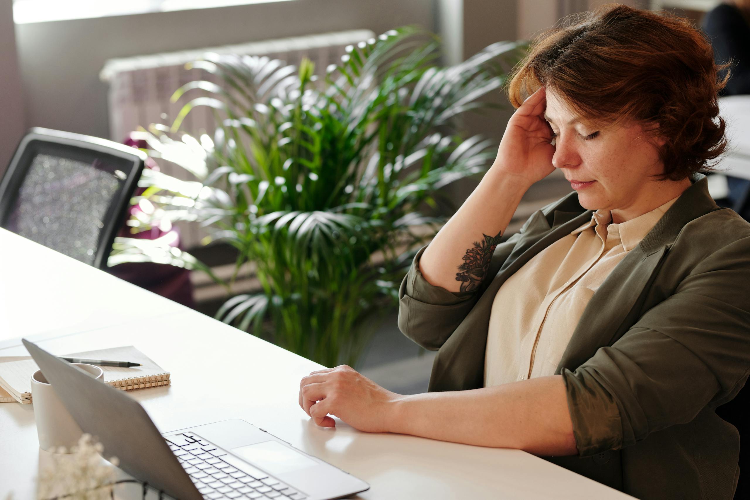 A businesswoman feeling stressed at her home office desk while working on her laptop.