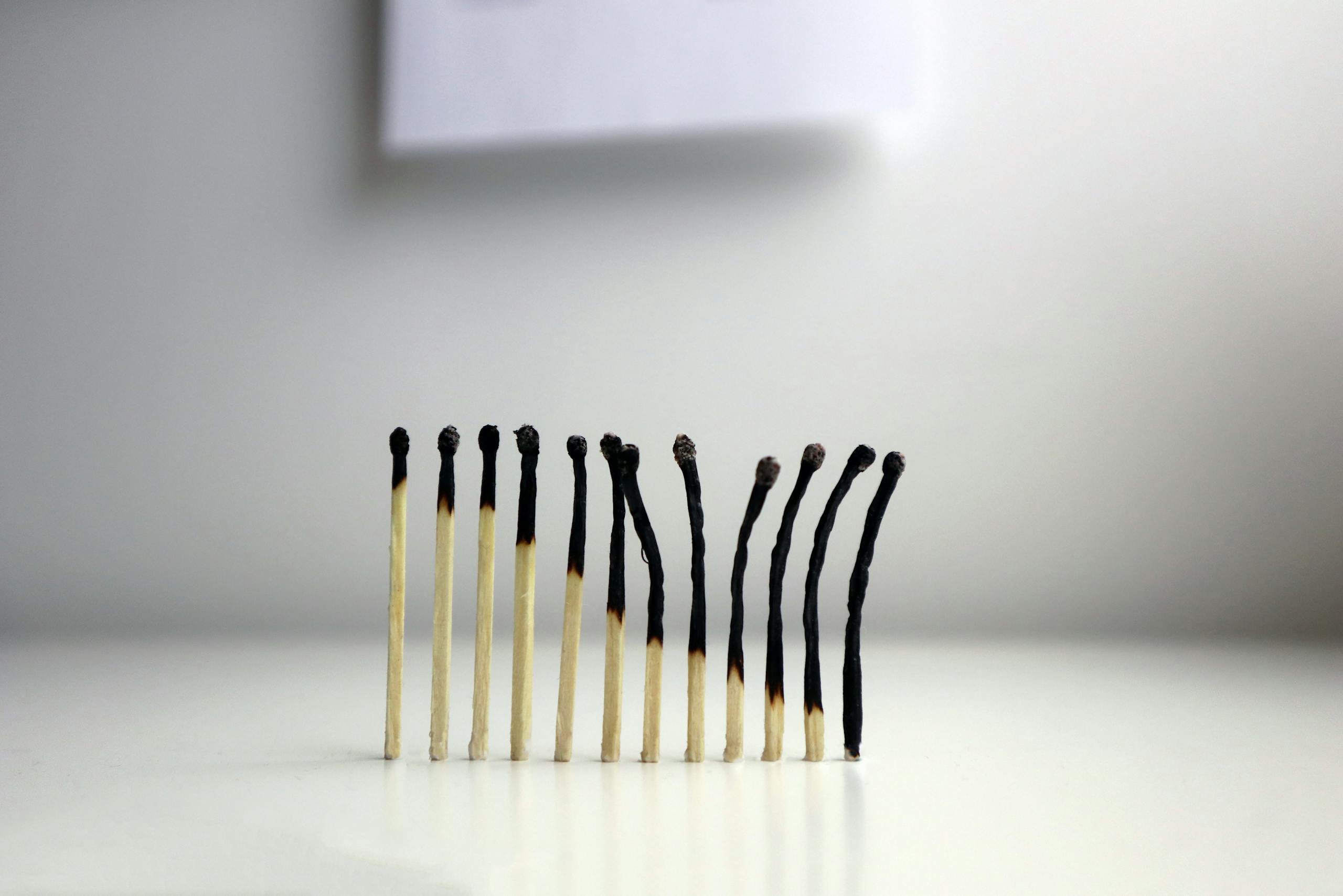 A row of burnt matches against a neutral background, representing burnout and exhaustion in a conceptual way.