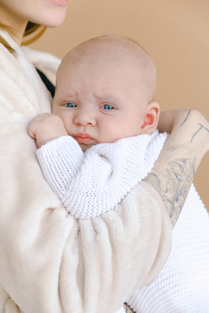 A tender moment of a mother gently holding her baby wrapped in a white knitted blanket indoors.