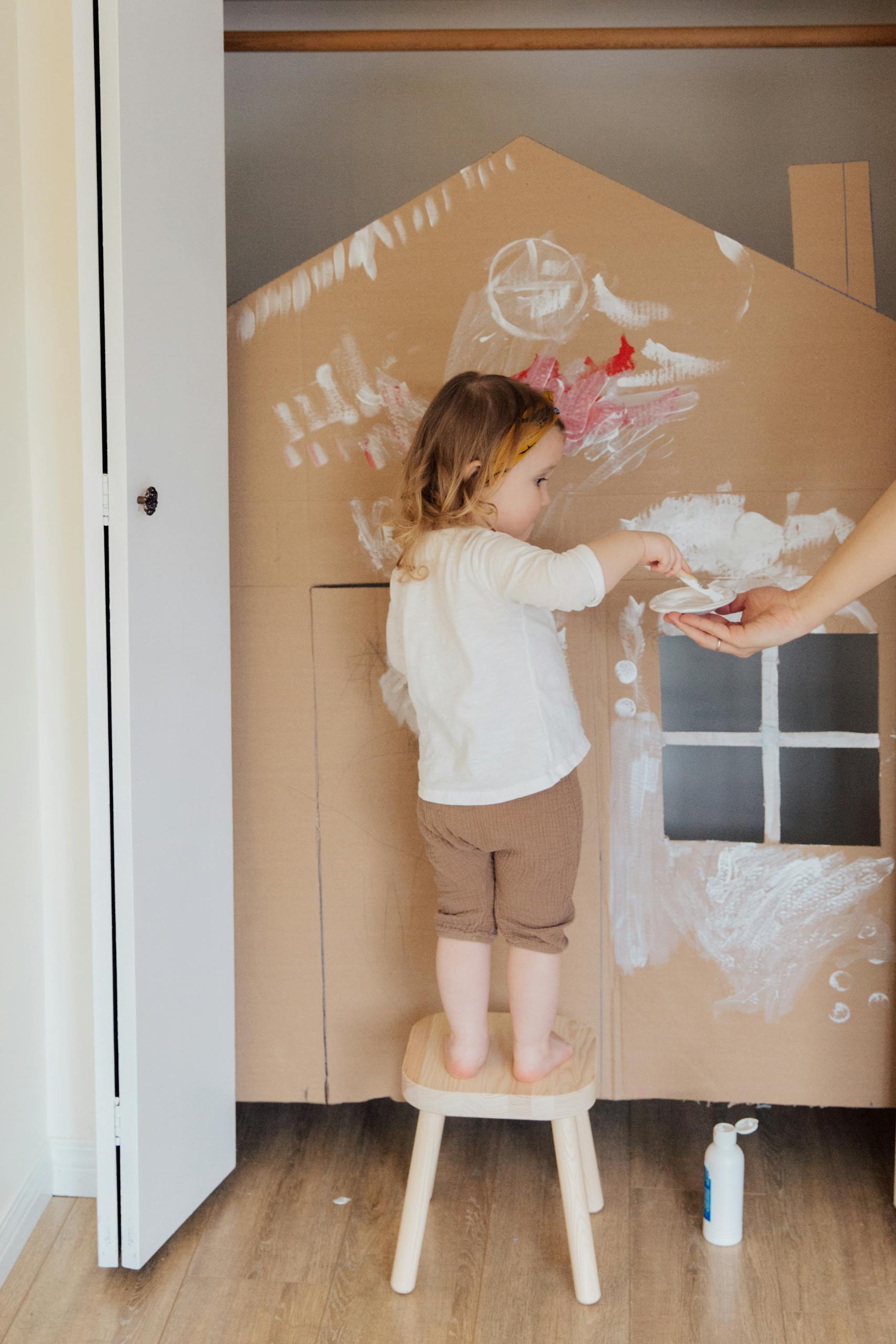 Child painting a cardboard house indoors with creativity and joy.