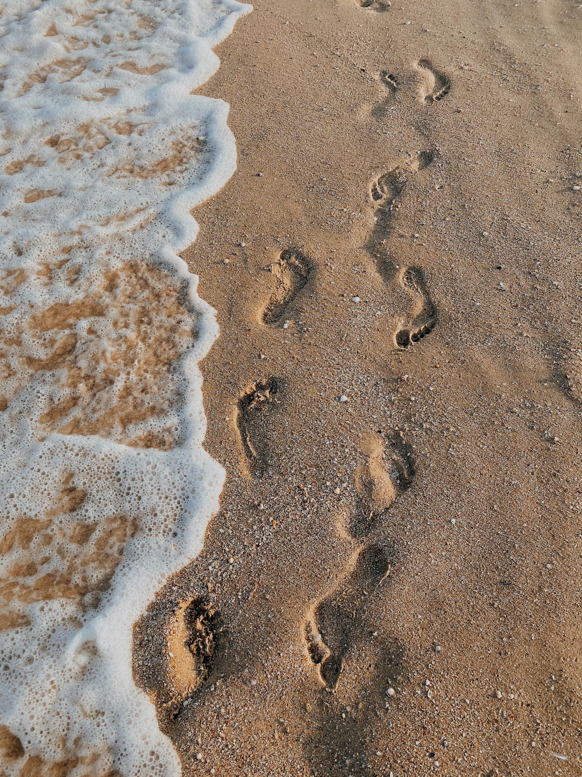 Coastal footprints on sandy beach with gentle waves, evoking peacefulness and travel vibes.